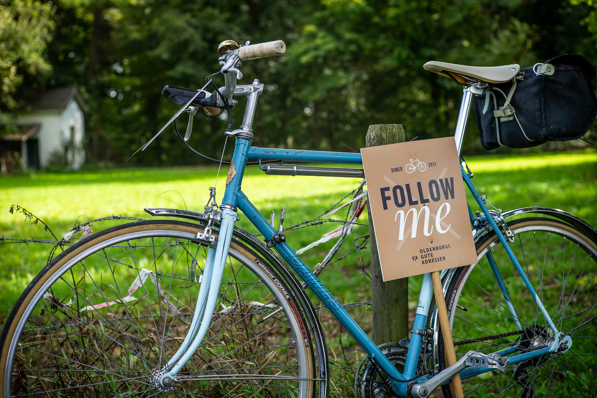 Ein blaues Vintage-Rennrad lehnt am „Follow me“-Wegweiser an der Strecke