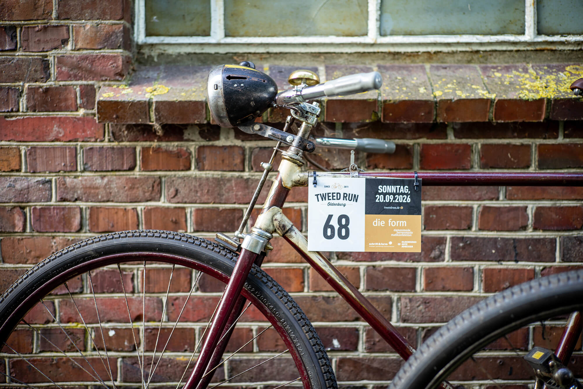 Weinroter Rahmen, alter Scheinwerfer und Starternummer 68 – historisches Fahrrad an der Backsteinmauer
